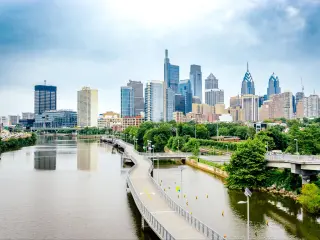 View of Philadelphia Skyline during daytime, with skyscrapers in background, river and greenery in foreground