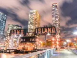 Long Island pier at night with lit-up skyscrapers behind the red and black sign
