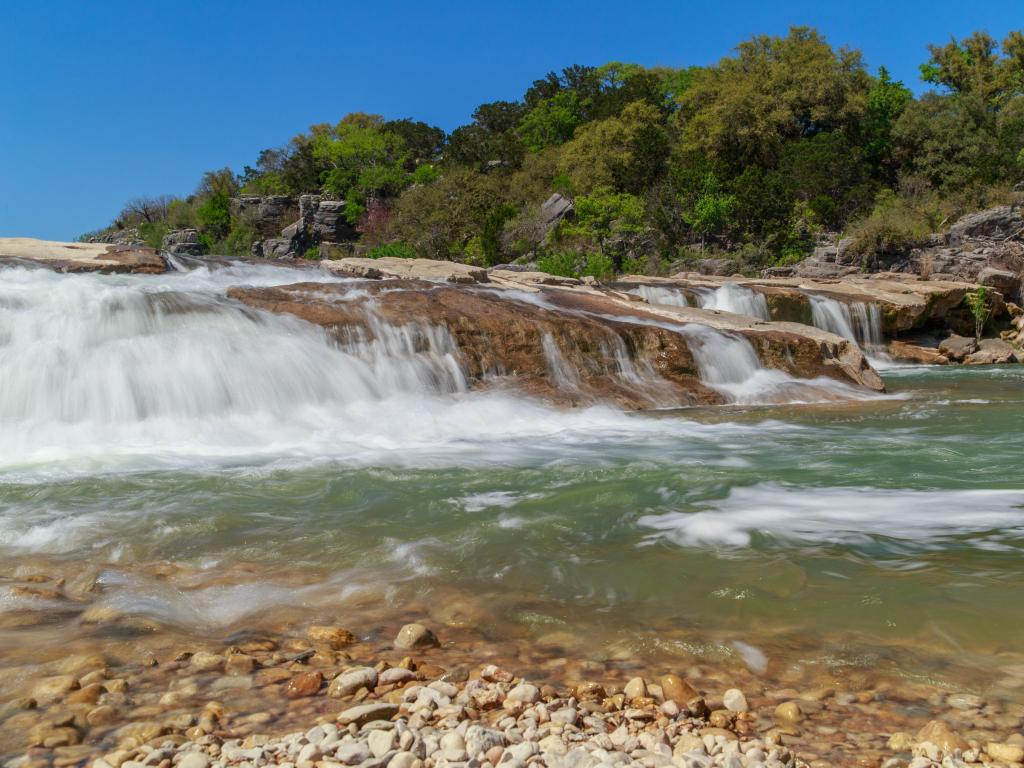 Light blue water flowing over rocks in a low, wide waterfall