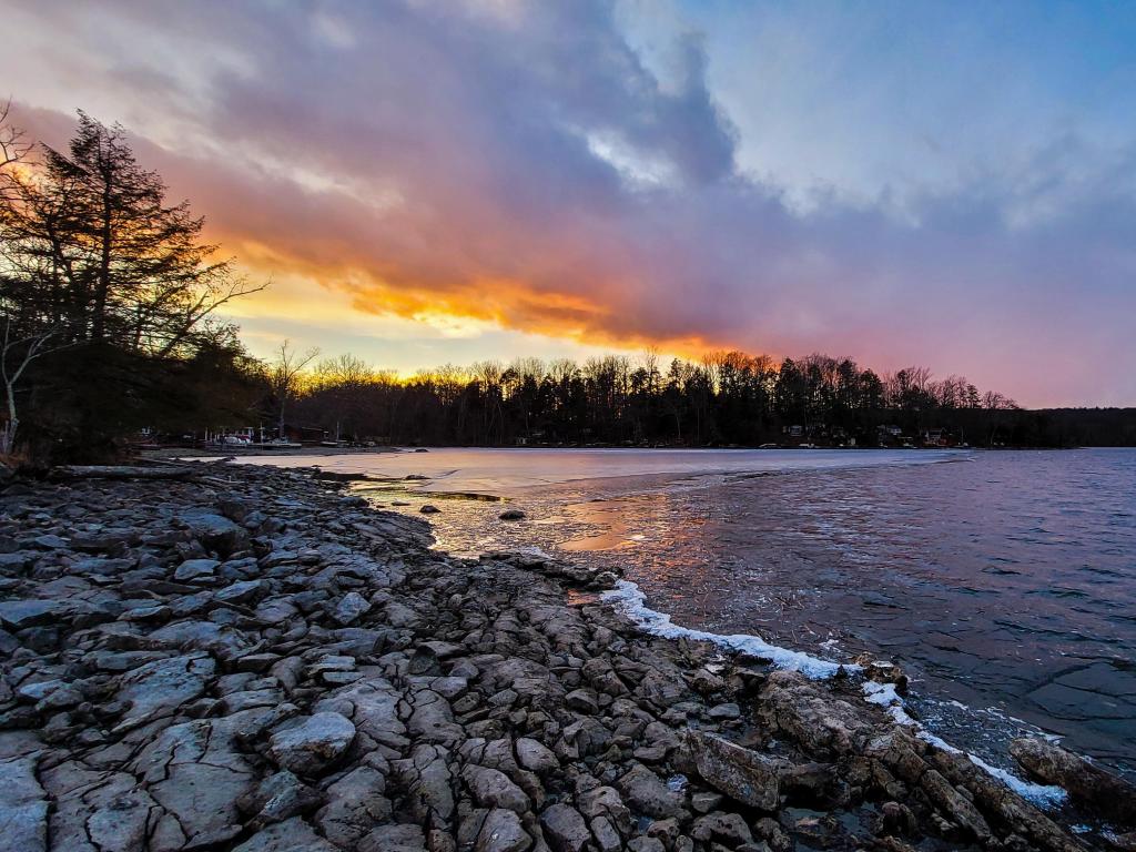 Stunning sunset across the waterfront in the background, and rocky shoreline across the forefront at Swartswood Lake in New Jersey.