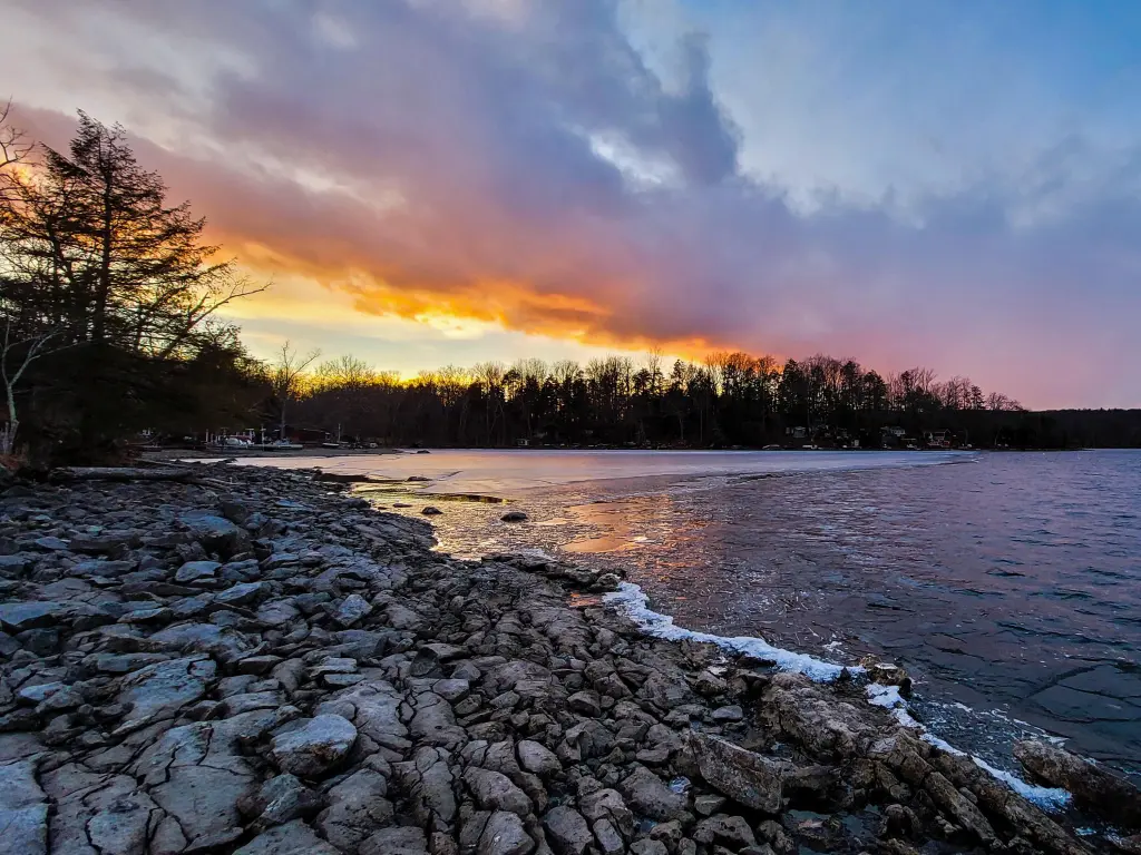 Stunning sunset across the waterfront in the background, and rocky shoreline across the forefront at Swartswood Lake in New Jersey.