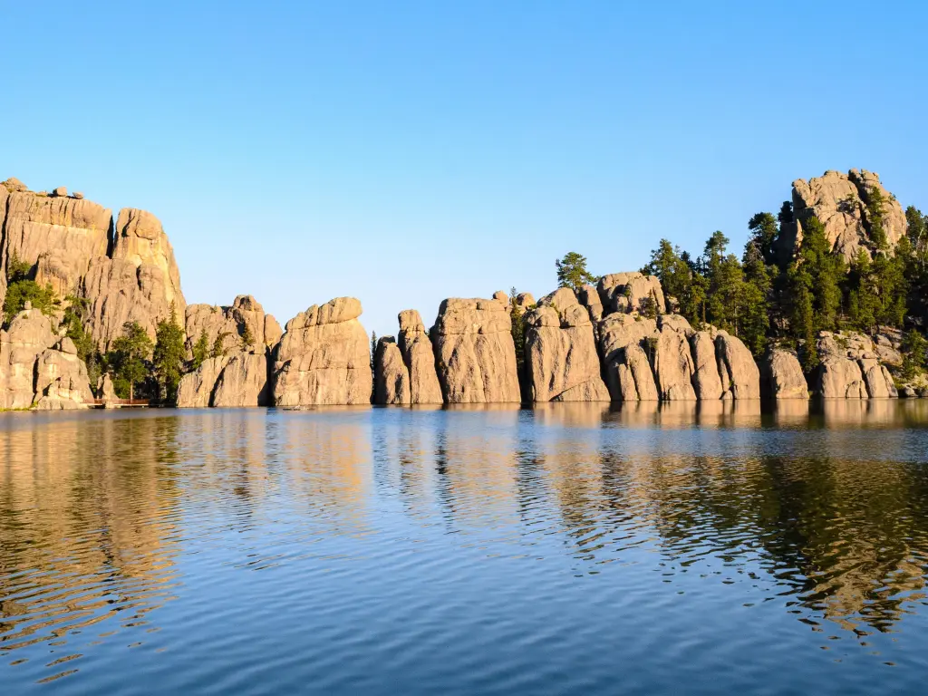 Panoramic view of Black Hills, reflected in the water, with lush forests across the hills in background and against blue skies.