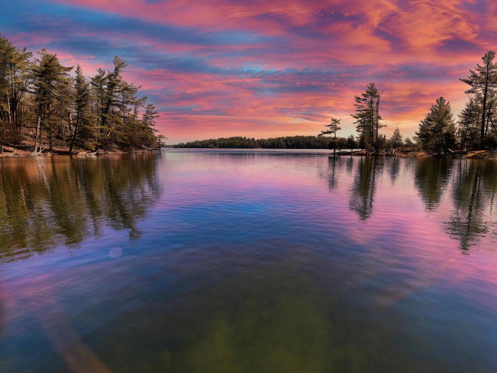 Charleston Lake Provincial Park, Ontario, Canada taken during a stunning sunsets with calm water in the foreground and trees lining the shores in the background. 