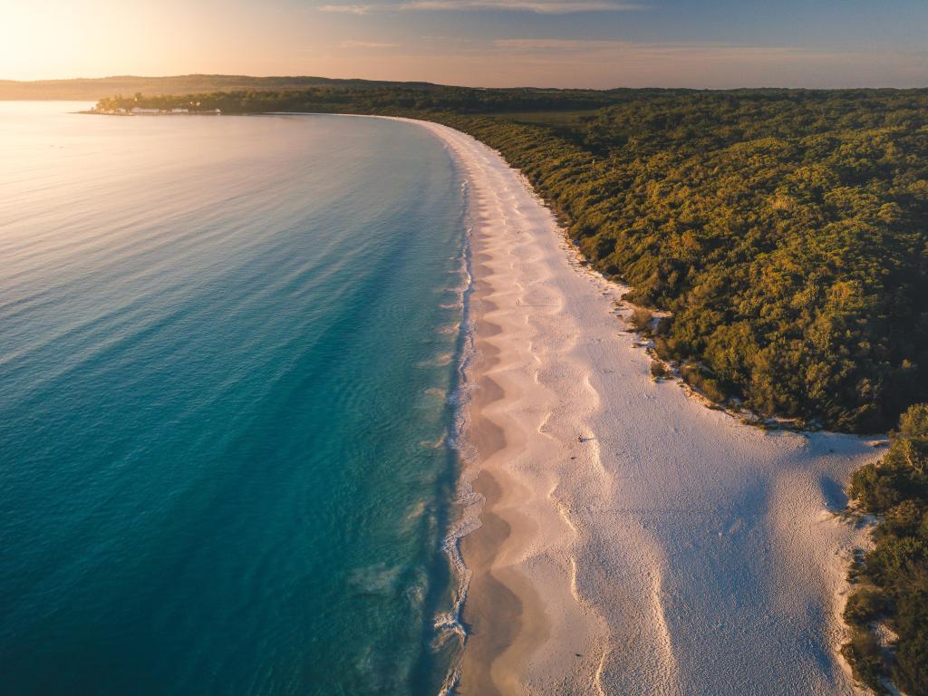 White sand and blue sea in hazy sunrise light with green vegetation along the shoreline