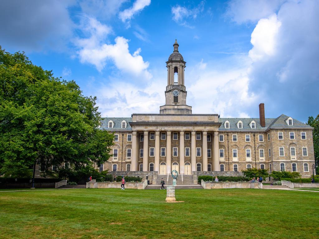 State College, Pennsylvania, USA with the Old Main building on the campus of Penn State University, taken on a sunny day with grass in the foreground.