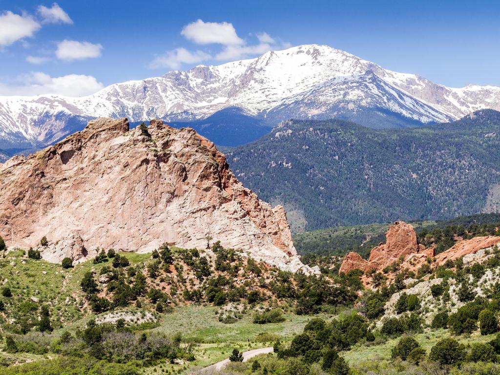 Colorado Springs, Colorado at the Garden of the Gods Park with mountains in the background covered in snow, and rocky mountains in the foreground below a blue sky.