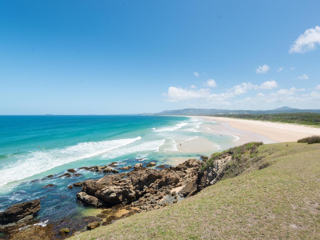 Coffs Harbour, NSW, Australia with a grass verge and cliffs and white sand and sea in the distance on a sunny day.