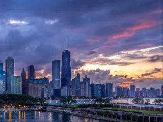 View of high rise buildings and lakefront with a grey cloudy sky and a hint of pink sunlight