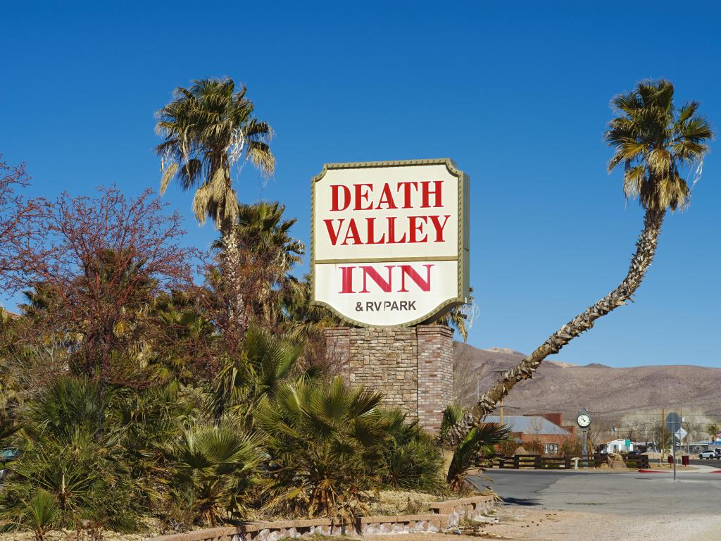 Large yellow and red sign at the entrance to Death Valley Inn, with desert, blue skies and palms in the background