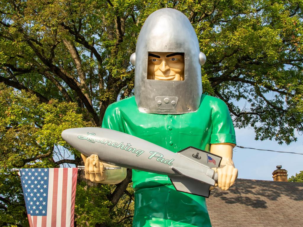 The statue of a man wearing a green shirt and a rocket helmet, while also holding a rocket