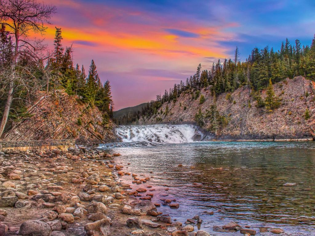 Bow Falls, Canada with a vibrant colorful Sky over the waterfall and river, rocky cliffs and trees in the distance. 