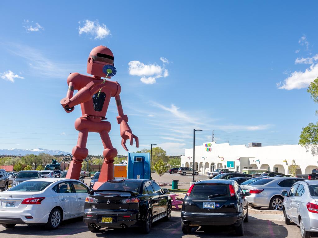A red robot statue in the parking lot of Meow Wolf on a sunny day