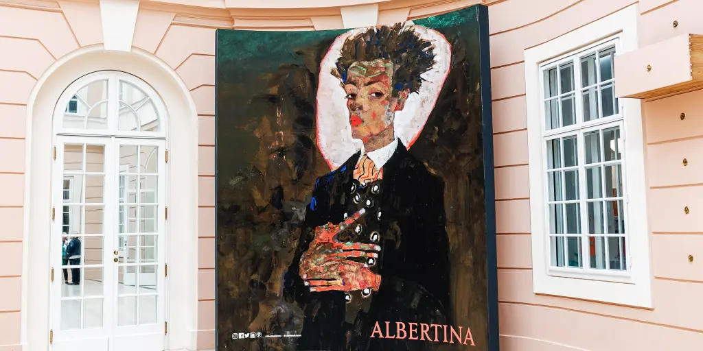 A painting of a man in a jazzy suit looking out towards the viewer, on a pink wall at the Albertina Museum, Vienna