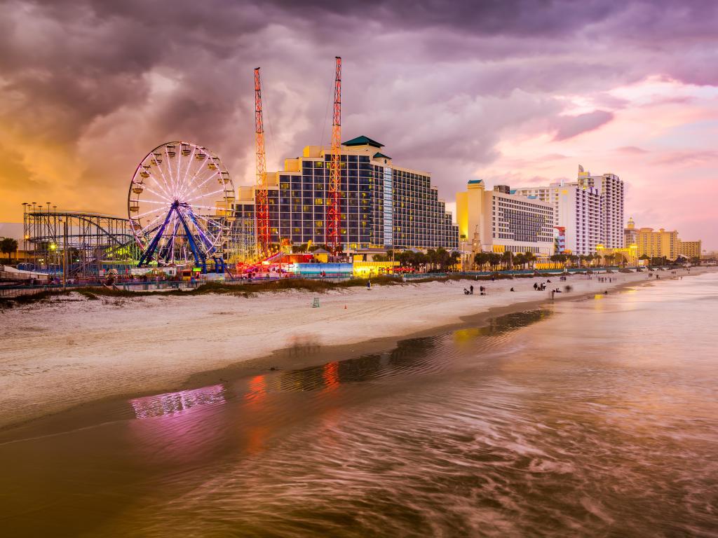 Daytona Beach, Florida, USA beachfront skyline with a ferris wheel and rides plus tall hotels in the background, the calm sea in the foreground taken early evening.