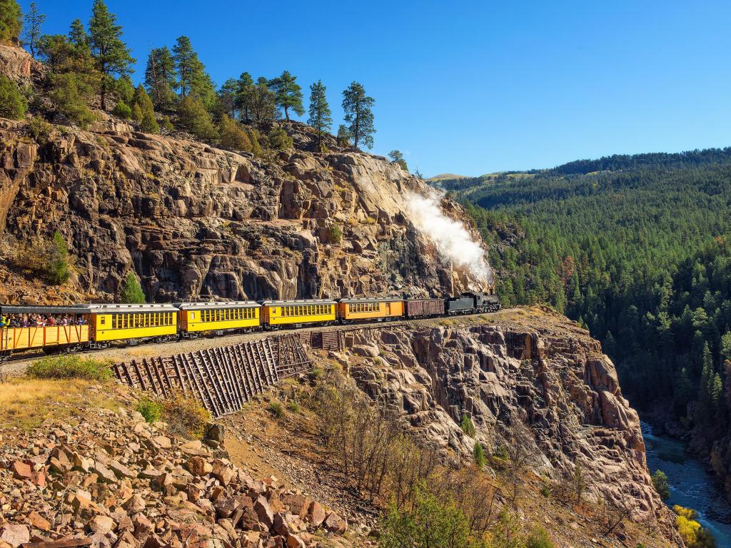 A historic steam train with yellow carriages runs through the San Juan Mountains Colorado