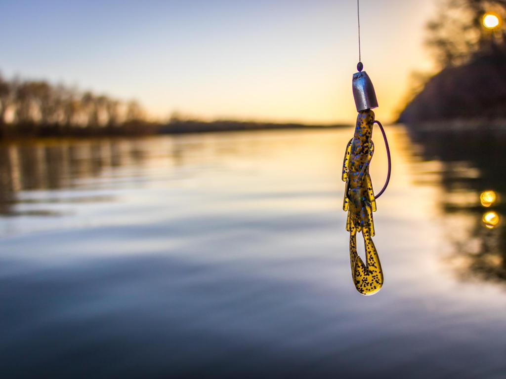 Fishing tackle held in the foreground at a lake at dusk