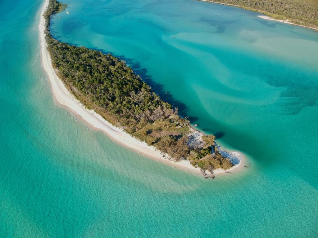 Small sandy island with green trees in turquoise water, viewed from above
