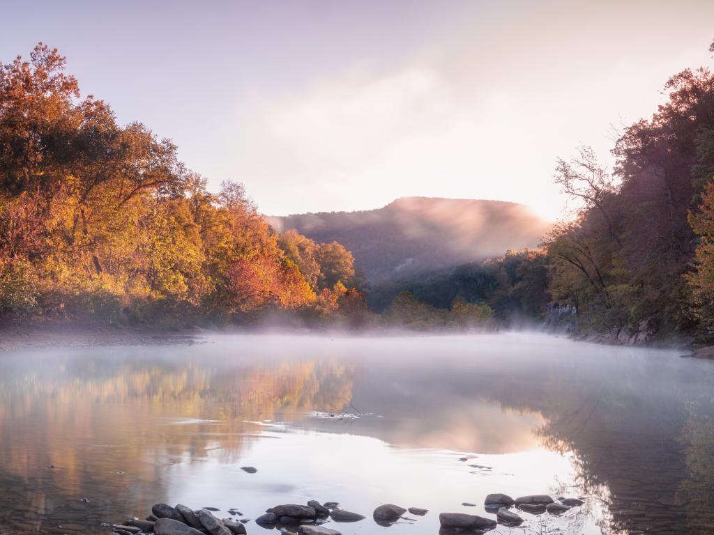 Ozark National Forest, USA with a foggy river in the foreground and trees in shades of reds and oranges in the background.