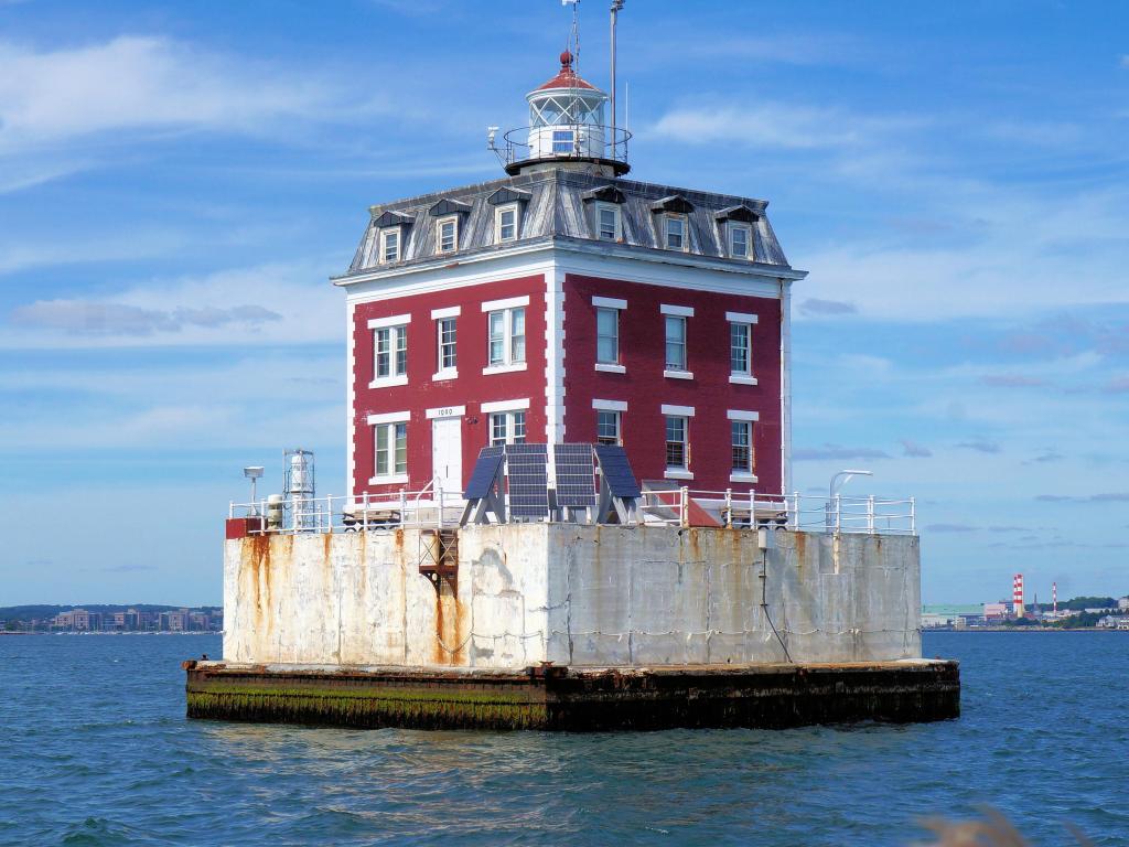 Square, red-brick lighthouse surrounded by water on a sunny day