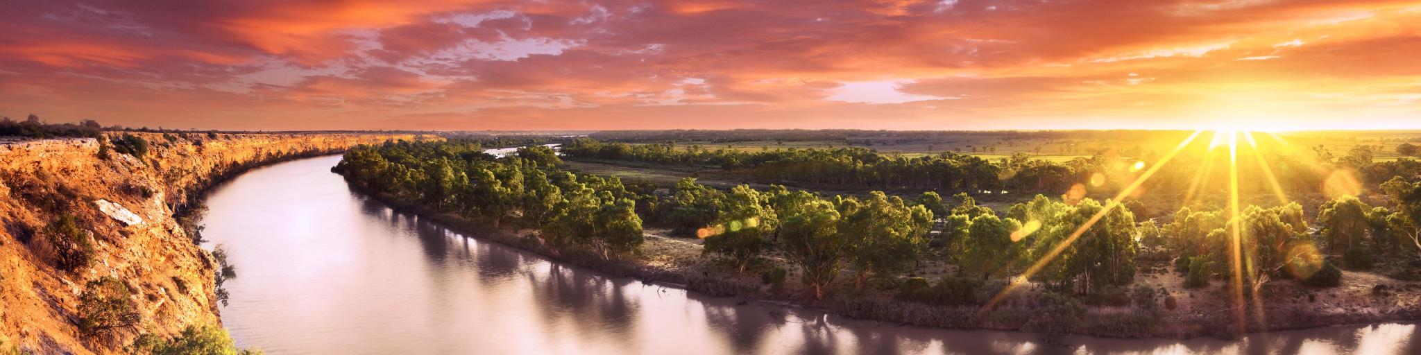 Pink sunset above calm Murray River with green trees on the banks