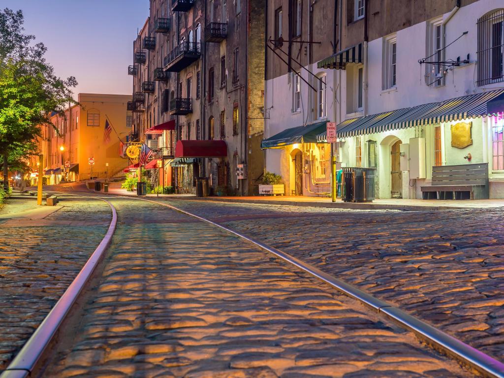 Tram line runs along cobbled street with low buildings, lit up in dawn light