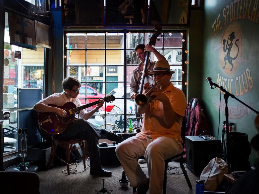 A group of musicians play in the dimly-lit Spotted Cat Bar in New Orleans, next to a window
