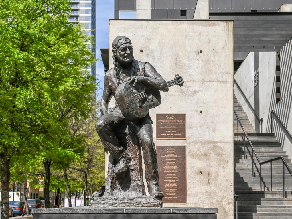 Sculpture of Willie Nelson in Austin Texas on a sunny day. The country musician is depicted as sitting and holding his guitar.