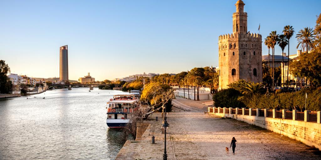 A woman walks her dog near the Torre del Oro in Seville, Spain, in winter