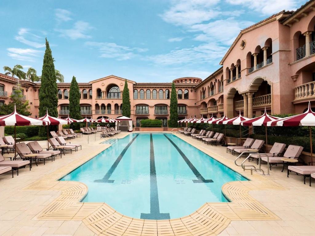 Stunning relaxation pool with loungers, and red and white patterned parasols along terrace, at Fairmount Grand Del Mar, San Diego