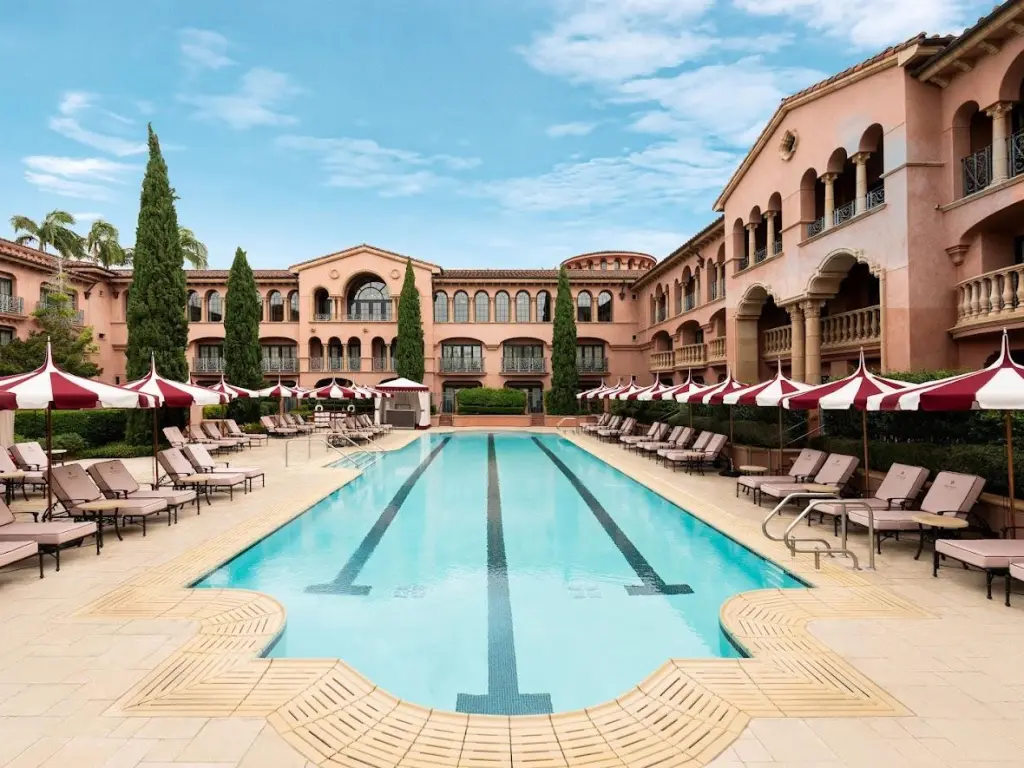 Stunning relaxation pool with loungers, and red and white patterned parasols along terrace, at Fairmount Grand Del Mar, San Diego
