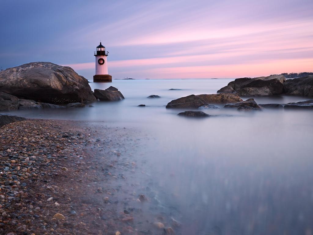 Fort Pickering Light, Salem, Massachusetts at dusk with calm water in the foreground and rocks in the distance. 