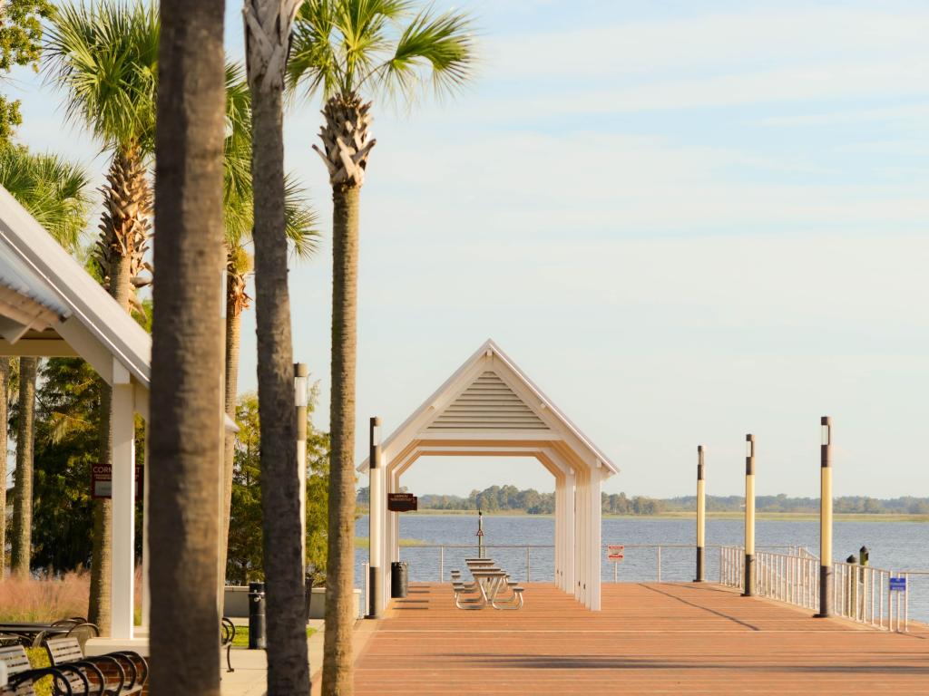 Boardwalk pier with picnic tables and benches under pavillions in the Kissimmee lakefront park with lake toho in the background and palms in the foreground