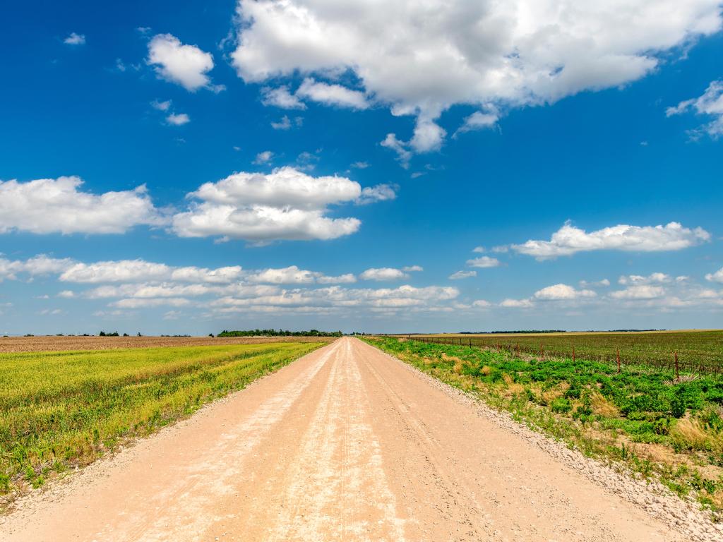 White clouds over a secluded dirt road stretching across the expansive flatlands of the Great Plains, Oklahoma