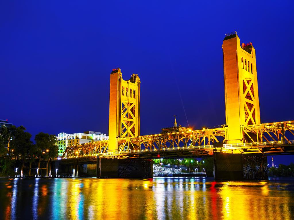 Golden Gates Drawbridge lit up in Sacramento at night time with the reflection in the water.