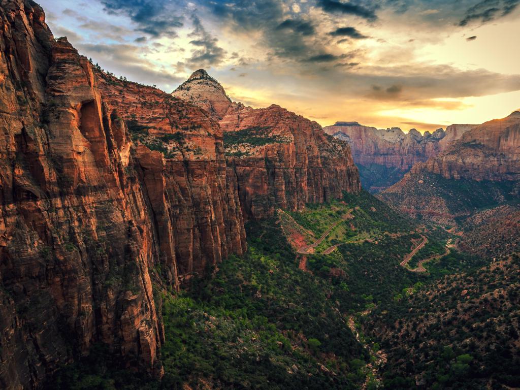 A tree-lined valley floor with a river just visible runs between tall, steep-sided rocky cliffs along a canyon