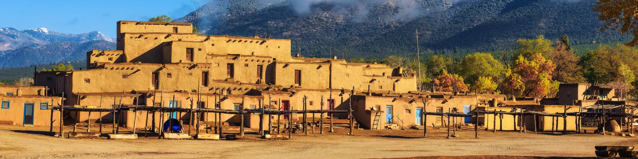 Ancient dwellings of Taos, with a hill in the background on a sunny day with a few clouds