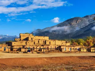 Ancient dwellings of Taos, with a hill in the background on a sunny day with a few clouds