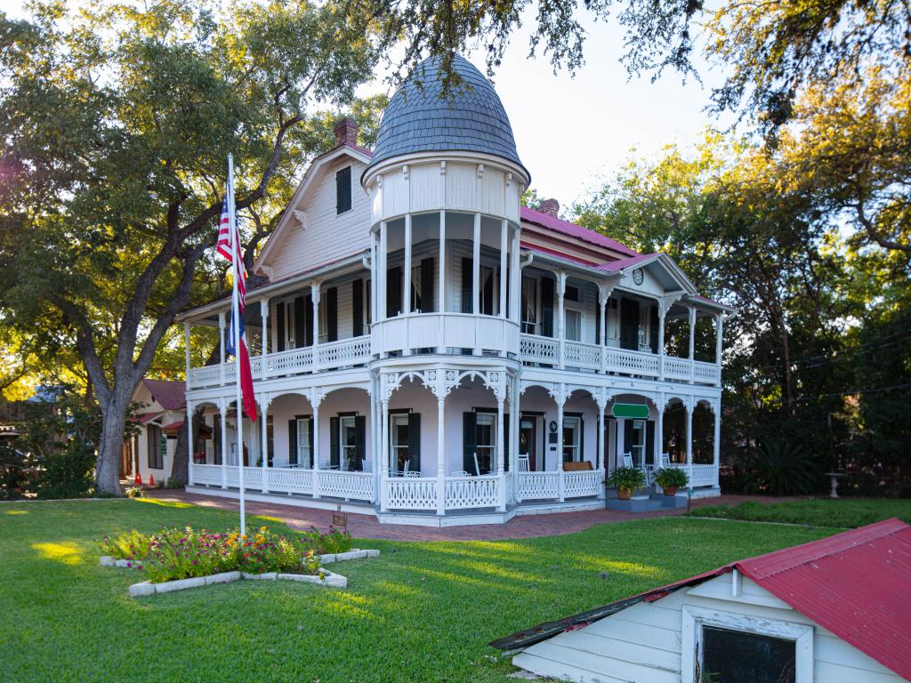 Historic Mansion in Gruene, Texas. There is a flag pole in front of the mansion, which is surrounded by green grass.
