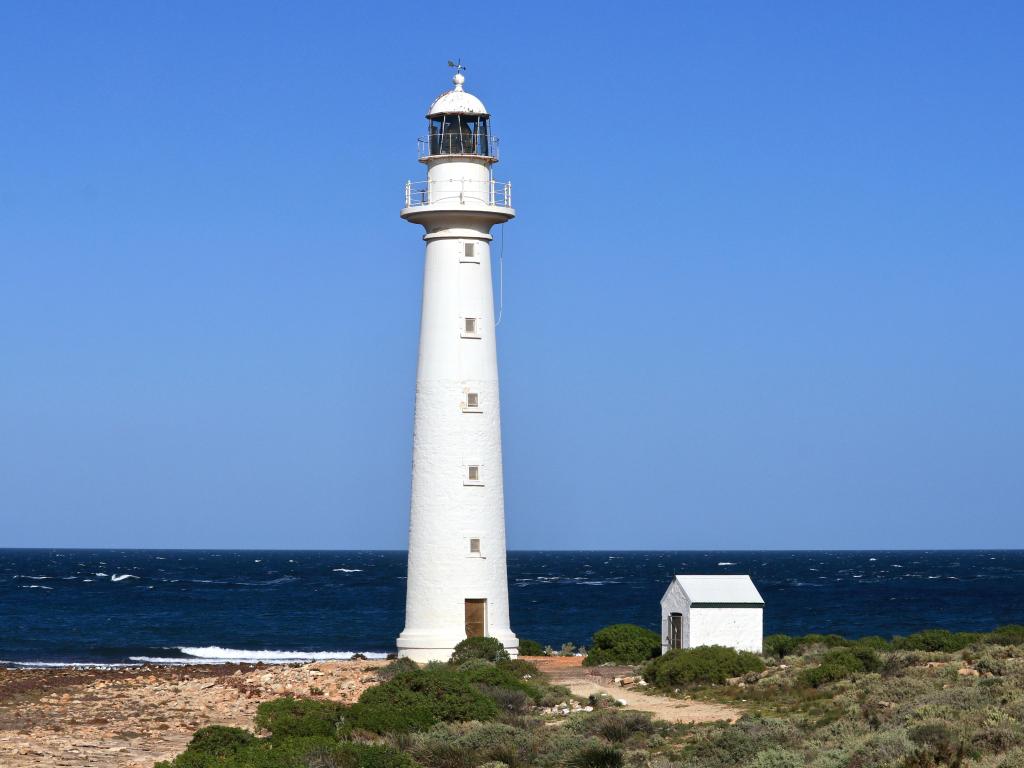 Abandoned lighthouse where the colorful outback meets the sea; sunny day and turbulent sea