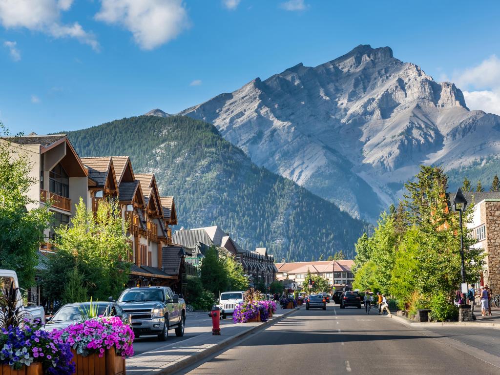 Banff, Alberta, Canada with a street and row of houses in the foreground and the stunning mountains in the distance on a sunny day.