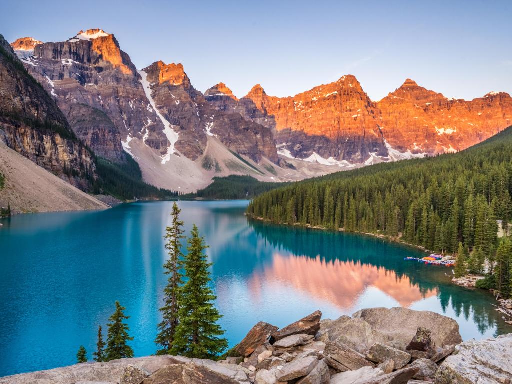 Banff National Park, Alberta, Canada with a sunrise over Moraine Lake in the foreground, trees in the distance and the beautiful mountains in the background. 
