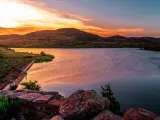 Wichita Mountain Wildlife Preserve, Oklahoma, United States with rock formations in the foreground, a large lake and mountains in the distance at sunset.