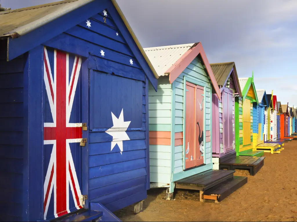 Beach houses painted in vibrant colours on a sandy beach, including one in the Australian flag