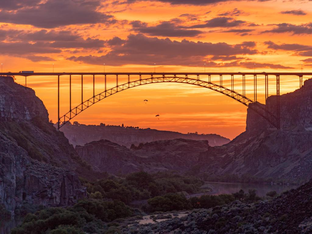 Bridge spans wide and deep river valley with steep rocky cliffs, in sunset light