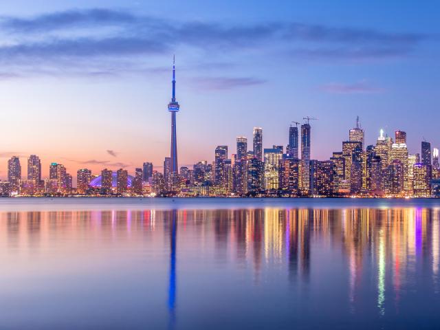 Toronto, Canada skyline with purple light and the city in the background reflecting in the water in the foreground.