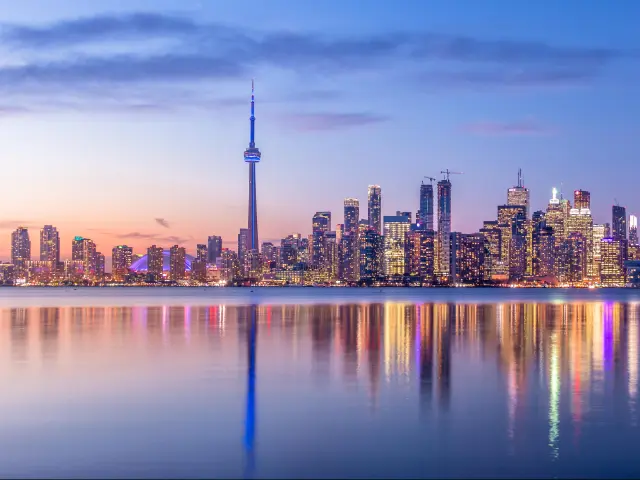 Toronto, Canada skyline with purple light and the city in the background reflecting in the water in the foreground.