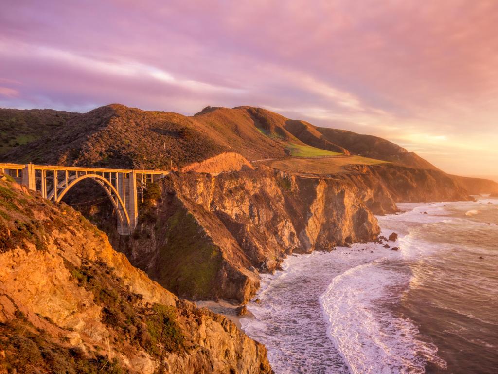 Purple hued sunset casting a warm glow on Bixby Bridge, Monterey, California