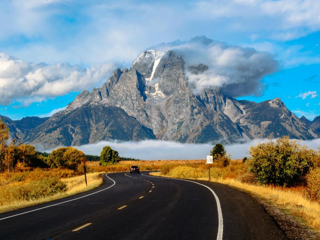 Road running towards Grand Teton National Park in Wyoming, USA, with mountains shrouded in clouds