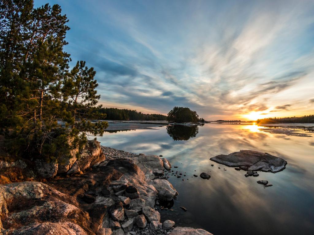 Voyageurs National Park, US/Canada border at sunset behind the Ash River Visitor Center (Minnesota) with calm waters surrounded by rocks and trees in the distance. 