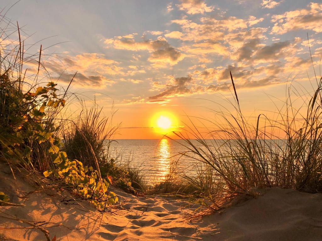 Vivid setting sun is reflected in silvery lake water, viewed in a gap between two dunes